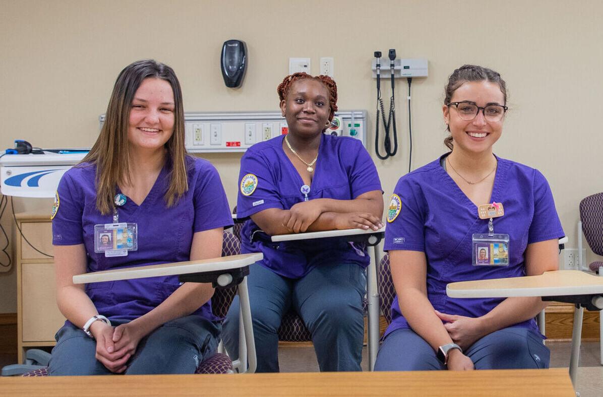 Three female nursing students smile while sitting at desks